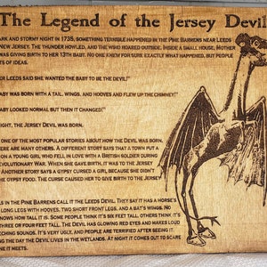 Puede incluir: Un letrero de madera con fondo marrón y texto negro cuenta la leyenda del Diablo de Jersey. El letrero presenta una ilustración en blanco y negro del Diablo de Jersey, una criatura con cabeza de caballo, alas de murciélago y patas largas con pezuñas. El texto del letrero describe al Diablo de Jersey como una criatura con ojos rojos brillantes y un chillido aterrador.
