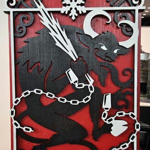 May include: A red wooden sign with a black silhouette of a chained creature with horns and a snowflake. The sign reads "Christmas Krampus".