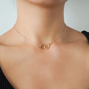 May include: A gold chain necklace with a handcuff pendant.