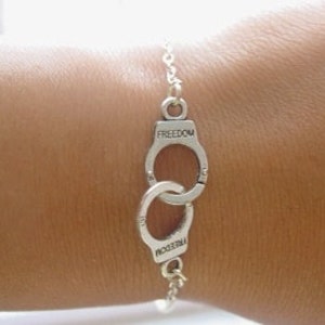 May include: Silver bracelet with two linked handcuff charms, each inscribed with the word "FREEDOM".
