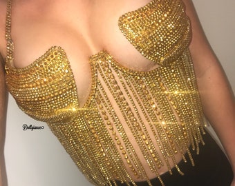 Könnte beinhalten: Ein goldfarbenes, mit Strass besetztes Oberteil mit Fransen. Das Oberteil hat einen tiefen V-Ausschnitt und besteht aus kleinen, glitzernden Strasssteinen.