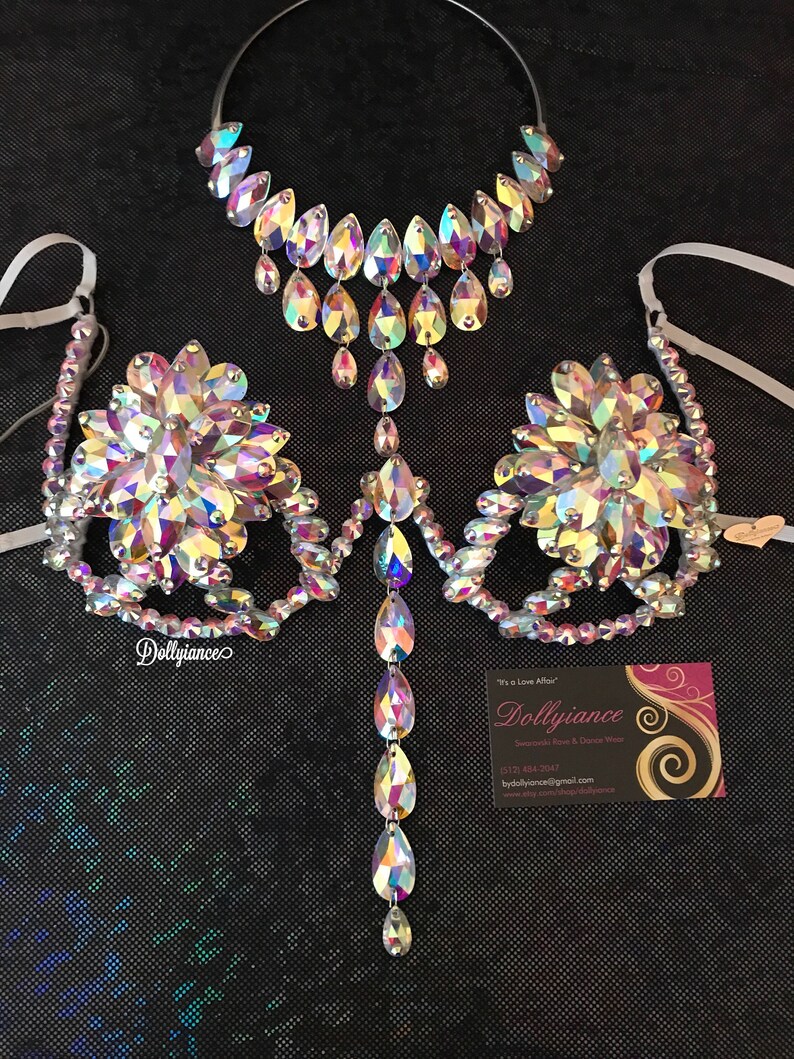 May include: A crystal rhinestone bra and necklace set. The bra has a floral design and the necklace is a teardrop design. The set is on a black background.