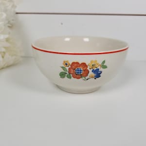 May include: A small, off-white ceramic bowl with a red rim and floral design. The flowers are in shades of orange, yellow, and blue with green leaves. The bowl is set against a white background.