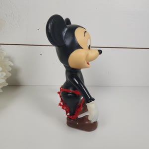 Puede incluir: Una figura vintage de Mickey Mouse de pl&aacute;stico negro y marr&oacute;n con pantalones cortos rojos. La figura est&aacute; de pie con los brazos a los lados.