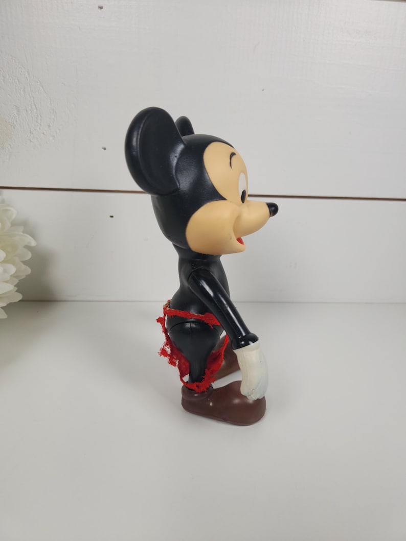 Puede incluir: Una figura vintage de Mickey Mouse de pl&aacute;stico negro y marr&oacute;n con pantalones cortos rojos. La figura est&aacute; de pie con los brazos a los lados.