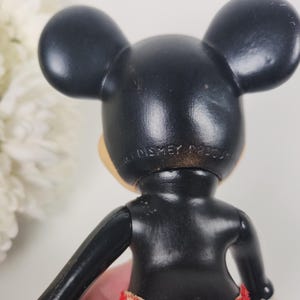 Puede incluir: Figurilla de Mickey Mouse de pl&aacute;stico negro con pantalones cortos de estampado rojo y blanco. La parte posterior de la figura tiene el texto "Walt Disney Product".