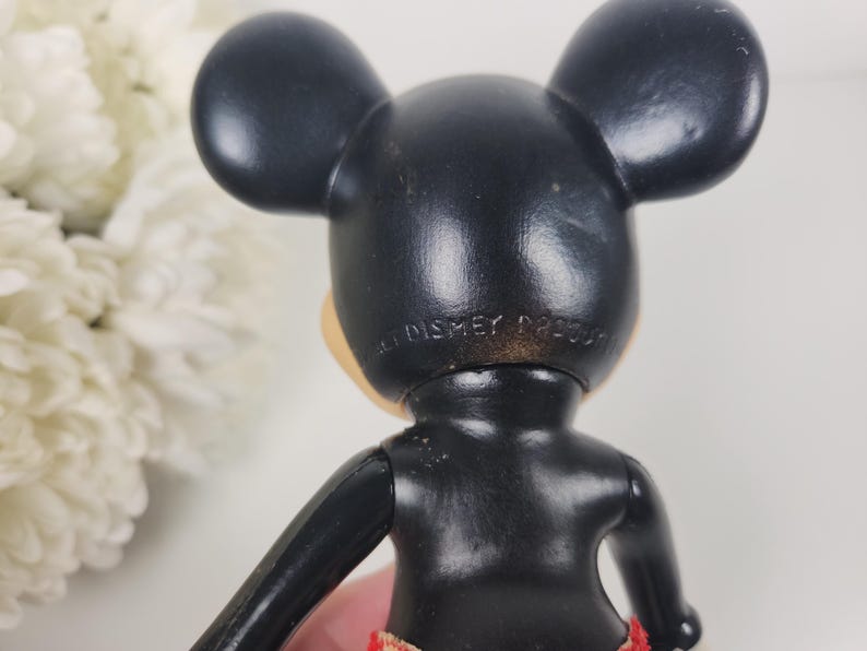 Puede incluir: Figurilla de Mickey Mouse de pl&aacute;stico negro con pantalones cortos de estampado rojo y blanco. La parte posterior de la figura tiene el texto "Walt Disney Product".