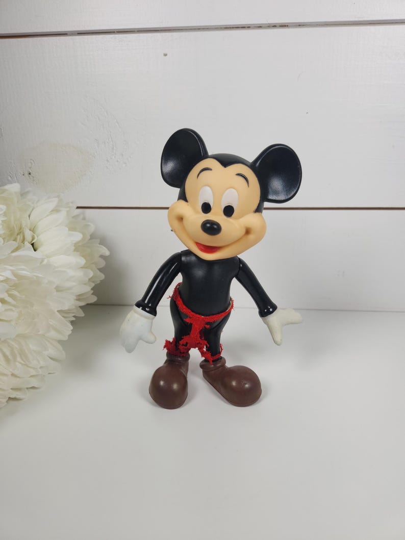 Puede incluir: Una figura vintage de Mickey Mouse de pl&aacute;stico negro con tela roja alrededor de la cintura. La figura tiene una cara sonriente con ojos negros y una nariz roja.