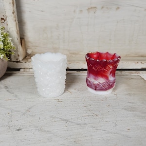 May include: Two small glass bud vases, one white and one red with white swirls. Both vases have a textured, raised design.