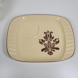 May include: A beige ceramic serving platter with a brown floral design and a divided section. The platter has a raised rim with a woven pattern.
