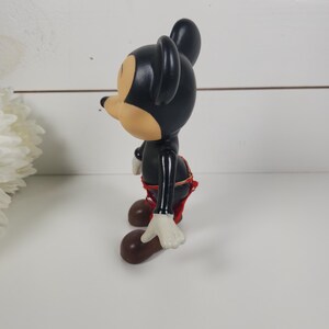 Puede incluir: Una figura vintage de Mickey Mouse en blanco y negro con pantalones cortos rojos y guantes blancos. La figura est&aacute; de pie sobre una superficie blanca.