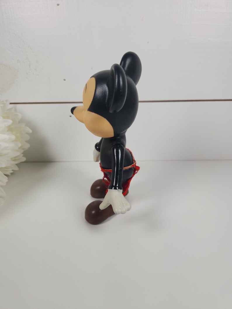 Puede incluir: Una figura vintage de Mickey Mouse en blanco y negro con pantalones cortos rojos y guantes blancos. La figura est&aacute; de pie sobre una superficie blanca.