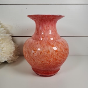 May include: A decorative, red and orange glass vase with a bulbous body and flared rim. The vase has a textured, mottled pattern and is approximately 8 inches tall.