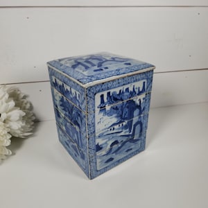 May include: A blue and white ceramic box with a square shape and a lid. The box is decorated with a traditional Chinese landscape scene.