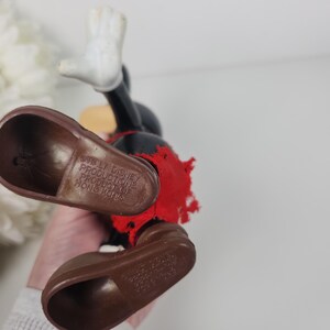 Puede incluir: Un juguete vintage de Mickey Mouse con zapatos marrones y una camisa roja. El juguete est&aacute; hecho de pl&aacute;stico y tiene una etiqueta en la parte inferior del zapato que dice "Walt Disney Productions Producto de Hong Kong".