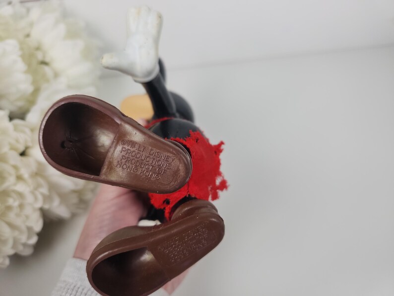 Puede incluir: Un juguete vintage de Mickey Mouse con zapatos marrones y una camisa roja. El juguete est&aacute; hecho de pl&aacute;stico y tiene una etiqueta en la parte inferior del zapato que dice "Walt Disney Productions Producto de Hong Kong".