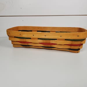 May include: A rectangular woven basket with a natural wood finish and colorful accents. The basket has a woven pattern with red, green, and blue accents.