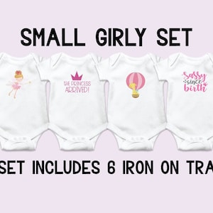 May include: Set of six iron-on transfers for baby onesies. The designs include a crown, a hot air balloon, a ballerina, a princess, a slipper, and the text "Daddy's Little Girl" and "Sassy Since Birth".