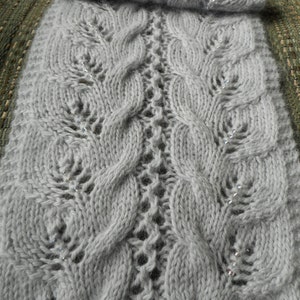 May include: A gray knitted scarf with a cable knit pattern and silver beads.