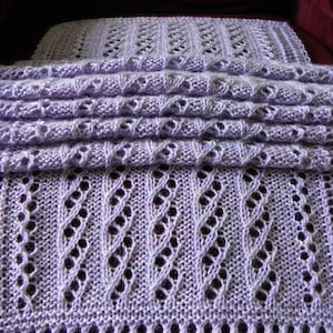 May include: A lavender knitted scarf with a delicate openwork pattern. The scarf is folded in half and laid flat on a burgundy surface.
