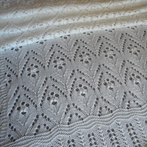 May include: White crocheted shawl with a delicate lace pattern. The shawl is folded in half and the lace pattern is visible on both sides.