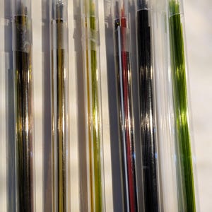 May include: A collection of thin, colorful rods in clear plastic tubes with blue caps. The rods vary in color, including black, gold, red, and green. The tubes are arranged in a row, suggesting a set of art supplies or craft materials.