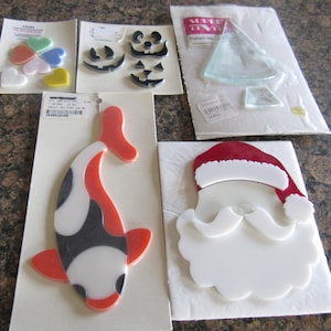 May include: Five sheets of stained glass window clings. The sheets feature a variety of designs, including hearts, a fish, a Santa Claus face, a Christmas tree, and jack-o-lantern faces.