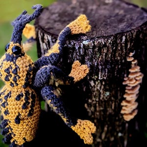 May include: A crocheted insect toy with a black and yellow patterned body. The toy is perched on a tree stump.