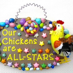 May include: A brown wooden sign with the text "Our Chickens are ALL-STARS" in yellow paint. The sign is decorated with colorful beads, stars, and a small yellow chicken figurine.