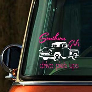 May include: A white decal on a red truck window with the text "Southern Girls drive pick ups". The decal features a black and white silhouette of a pickup truck.