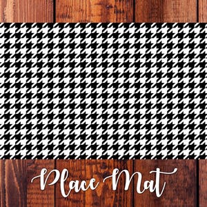 May include: Black and white houndstooth patterned place mat. The place mat is rectangular and has a smooth surface.