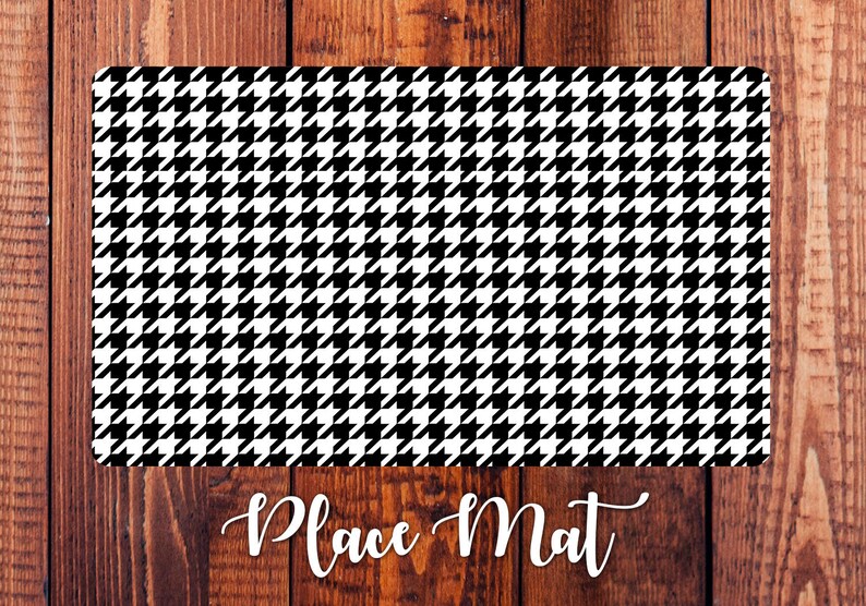 May include: Black and white houndstooth patterned place mat. The place mat is rectangular and has a smooth surface.