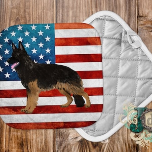 May include: A white and gray quilted hot pad with a red, white, and blue American flag design featuring a German Shepherd dog.