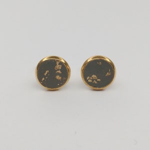 May include: A pair of gold stud earrings with a dark gray background and gold flecks.