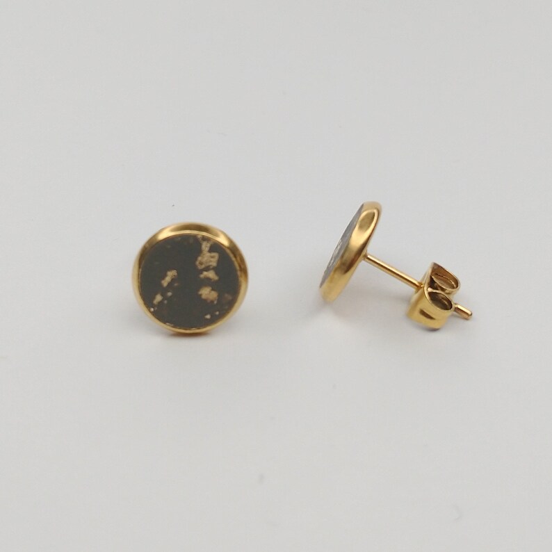 May include: A pair of gold stud earrings with a round black and gold design. The earrings are made of metal and have a simple, elegant design.