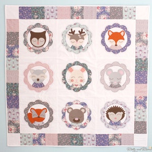 May include: A white baby quilt with a patchwork border featuring floral patterns in shades of purple, pink, and green. The centre of the quilt features nine appliqued animal faces, including an owl, deer, fox, raccoon, bunny, mouse, fox, bear, and hedgehog, each surrounded by a scalloped circle.