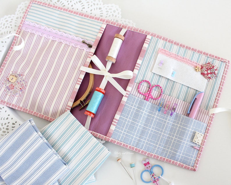 May include: A pink and blue striped fabric organizer with multiple pockets and compartments. The organizer is filled with sewing supplies, including scissors, thread, needles, and a hoop.