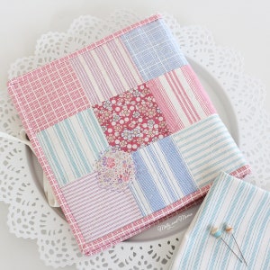 May include: A patchwork fabric book cover with a pink, blue, and white striped pattern. The cover is made of different fabrics with floral prints. The text "Molly and Mama" is visible on the bottom right corner.
