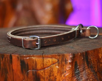 May include: A brown leather dog collar with white stitching and a silver buckle. The collar is on a wooden surface.