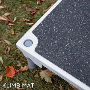 May include: White pet step with a black textured surface and grey plastic feet. The step has a grey plastic cap on the corner. The text "KLIMB MAT" is visible in the bottom left corner of the image.
