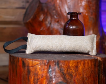 May include: A beige canvas dog chew toy with a black handle. The toy is sitting on a wooden stump with a brown glass bottle behind it.