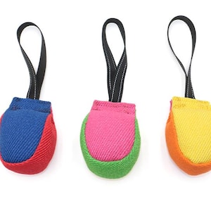 May include: Three dog toys in vibrant colours, each with a loop. The toys are in red and blue, pink and green, and yellow and orange. They are made from a textured fabric and are designed for play.