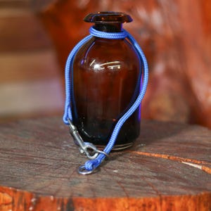 May include: A brown glass bottle with a blue rope tied around it and a silver hook attached to the rope.