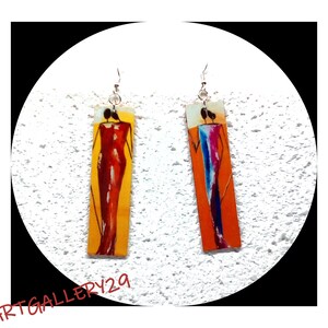 Puede incluir: Un par de pendientes colgantes con figuras abstractas coloridas en piezas metálicas rectangulares. Las figuras están pintadas en tonos de rojo, naranja, azul y amarillo.