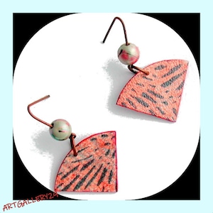 Peut inclure: Une paire de boucles d'oreilles avec un motif en forme d'éventail. Les boucles d'oreilles sont en métal et ont un motif rose et noir. Chaque boucle d'oreille a une petite perle ronde verte.