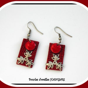 Puede incluir: Pendientes de cuero rojo con detalles florales plateados y un círculo rojo en el centro. Los pendientes están etiquetados como "Boucles d'oreilles HANGLARI".