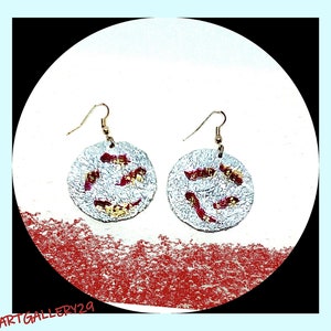 Peut inclure: Une paire de boucles d'oreilles argentées avec des accents rouges et dorés. Les boucles d'oreilles sont rondes et ont une surface texturée.