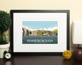 Puede incluir: Una impresión enmarcada en negro con un passe-partout blanco. La impresión presenta una ilustración colorida de un puente y una ciudad con el texto "Knaresborough, North Yorkshire, England".