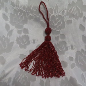 May include: A red beaded tassel with a loop at the top and two round beads at the bottom.