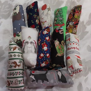 May include: A collection of cat toys in various festive patterns. Designs include cats, Christmas trees, Santa Claus, and holiday motifs. The toys are rectangular and made of fabric, perfect for feline fun.